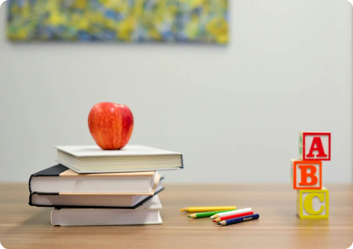 A stack of books with an apple and lettered blocks beside them